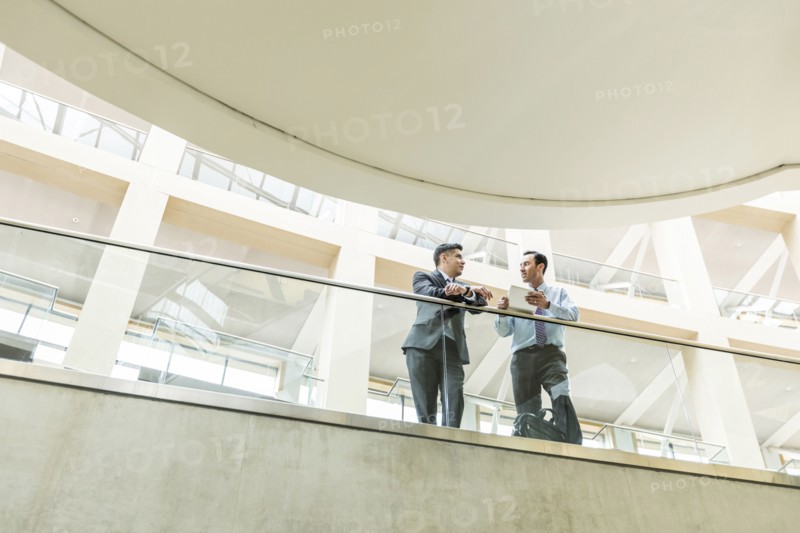 Mixed Race businessmen talking in lobby using digital tablet