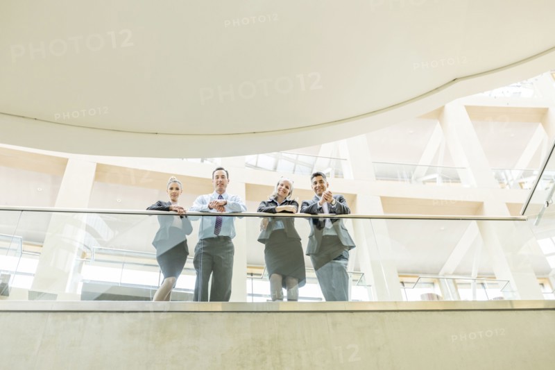 Portrait of smiling business people leaning on railing in lobby