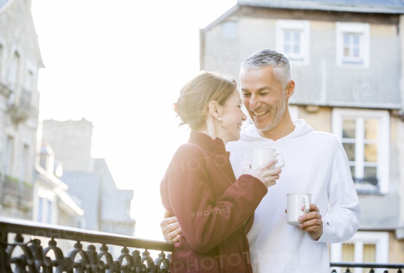 Caucasian couple drinking coffee on balcony in city