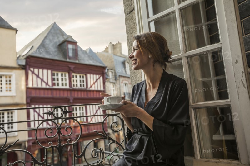 Caucasian woman drinking coffee on balcony in city