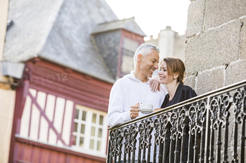 Caucasian couple drinking coffee on balcony in city