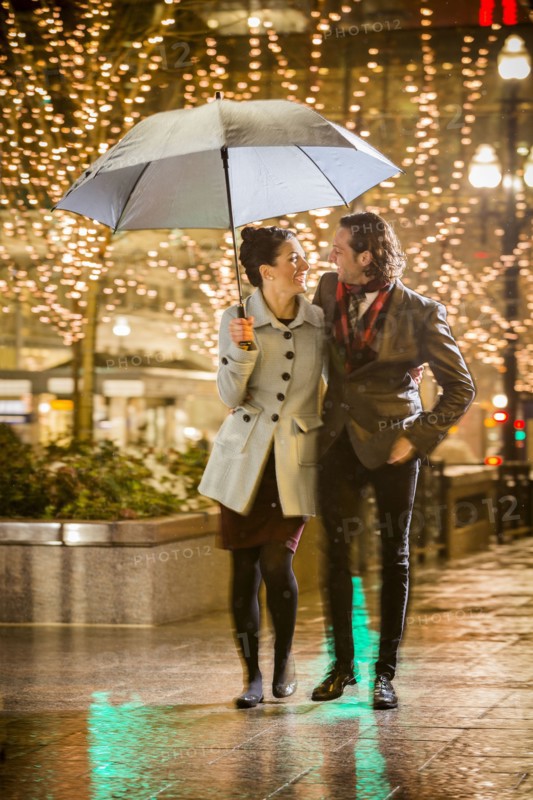 Caucasian couple carrying umbrella in city at night
