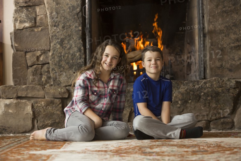 Smiling Caucasian brother and sister sitting on floor near fireplace