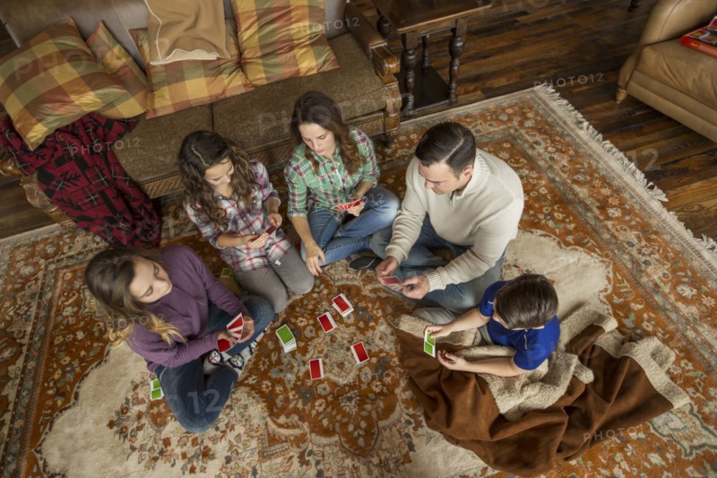 Caucasian family sitting on rug playing card game
