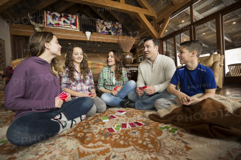Caucasian family sitting on rug playing card game