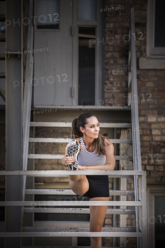 Caucasian woman stretching leg on urban staircase