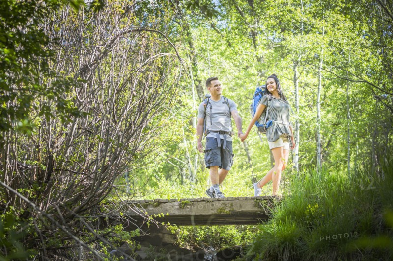 Couple carrying backpacks across bridge in woods