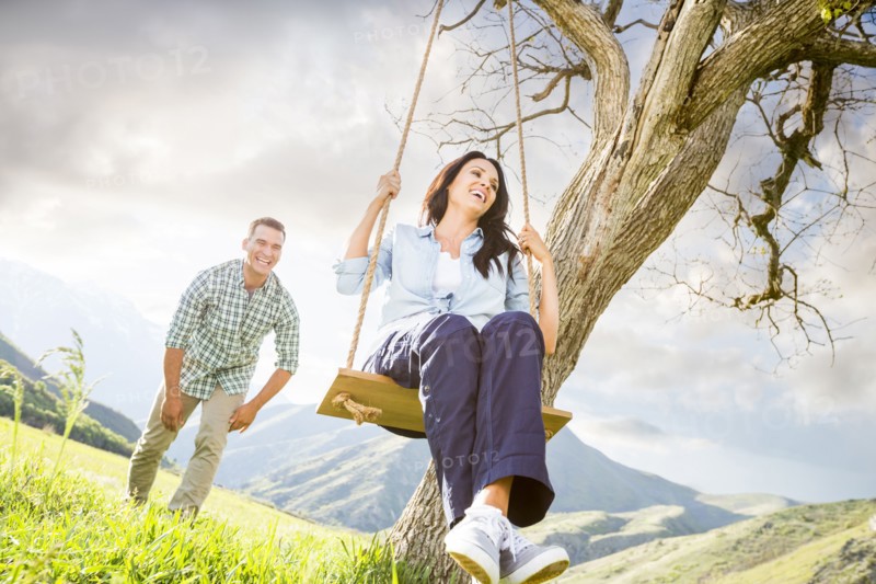 Man pushing woman swinging on tree swing