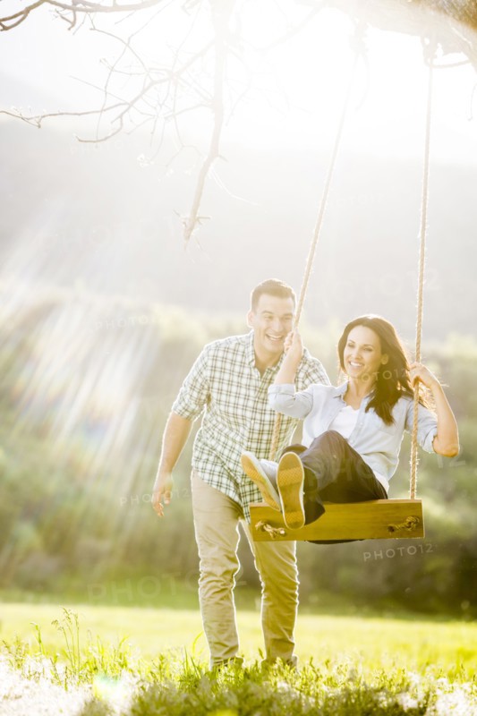 Man pushing woman swinging on tree swing