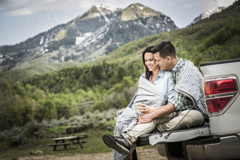Couple wrapped in blanket sitting on bed of pick-up truck