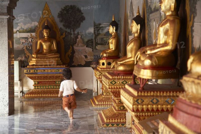 Mixed race child running past Buddha statues