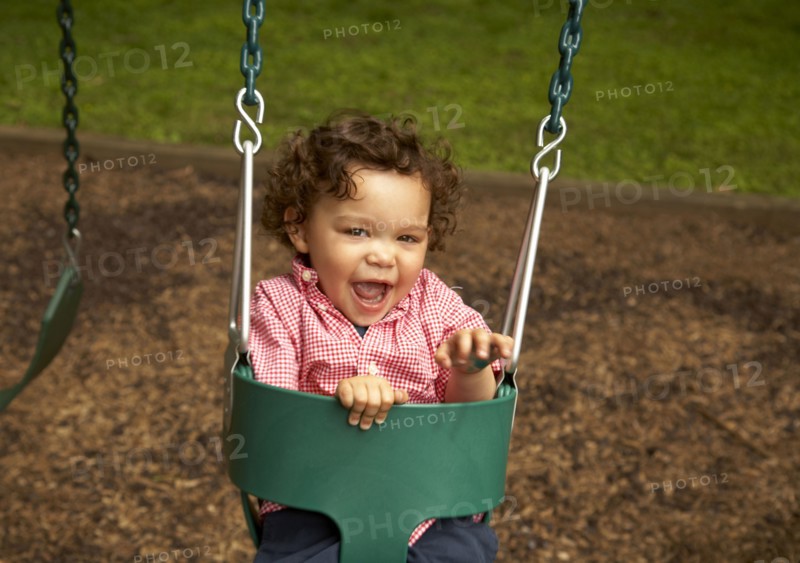 Mixed race child sitting in swing laughing