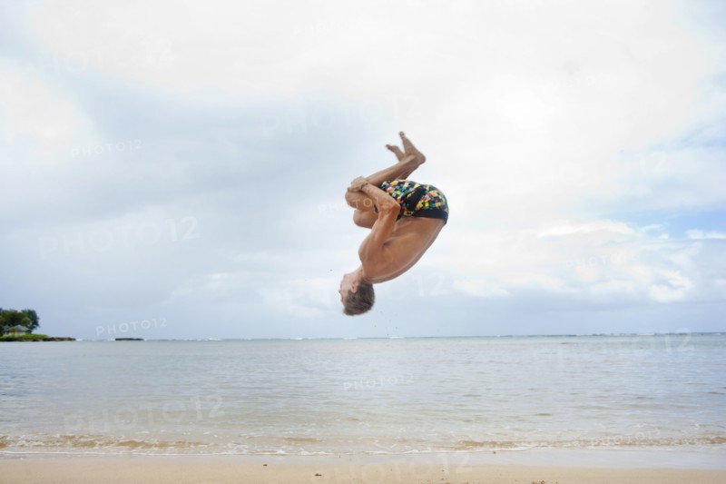 Caucasian man doing a flip on beach