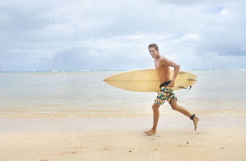 Caucasian man running on beach carrying surfboard