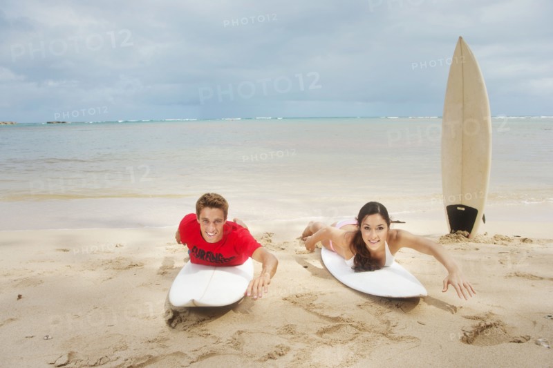 Couple laying on surfboards on beach