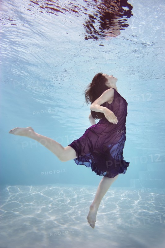Caucasian woman in dress swimming underwater