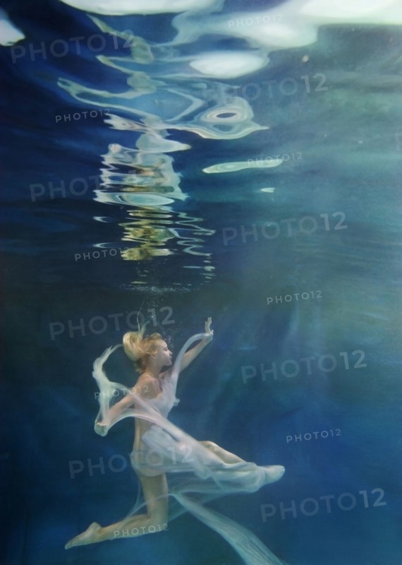 Caucasian woman in dress swimming under water