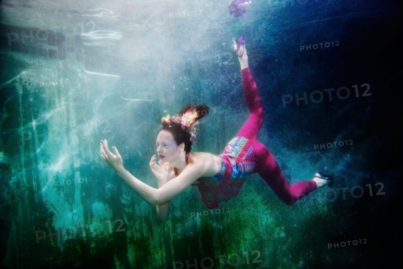 Caucasian woman in clothing swimming under water