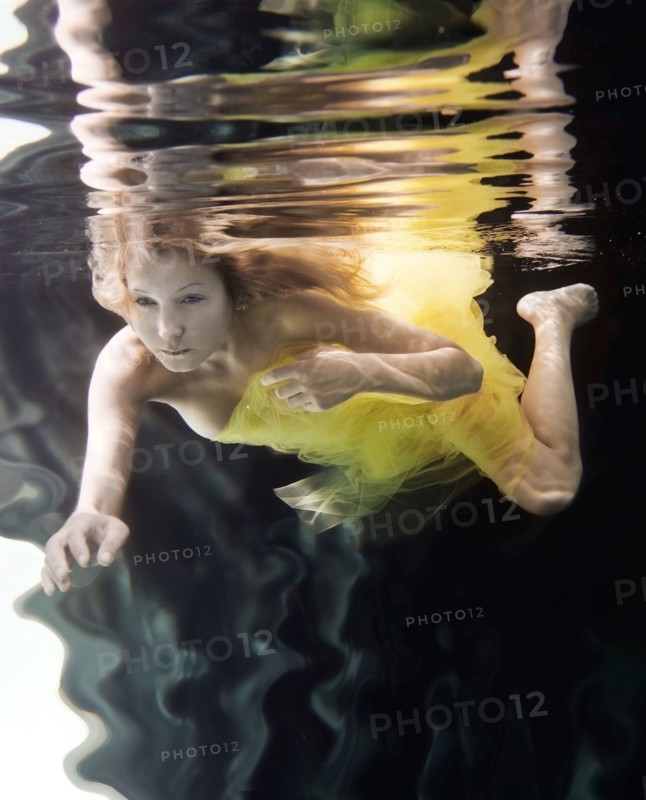 Caucasian woman in dress swimming under water