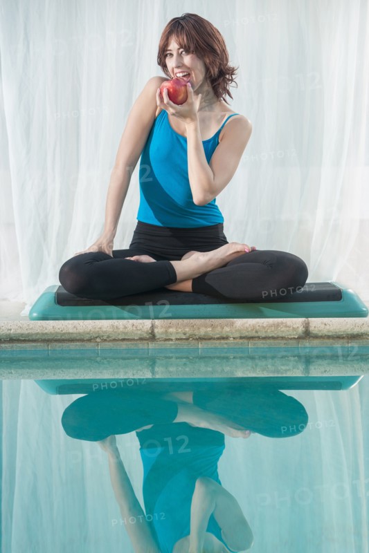 Mixed race woman eating apple near swimming pool