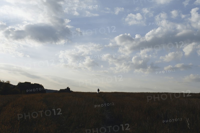 Distant Caucasian man in field under clouds