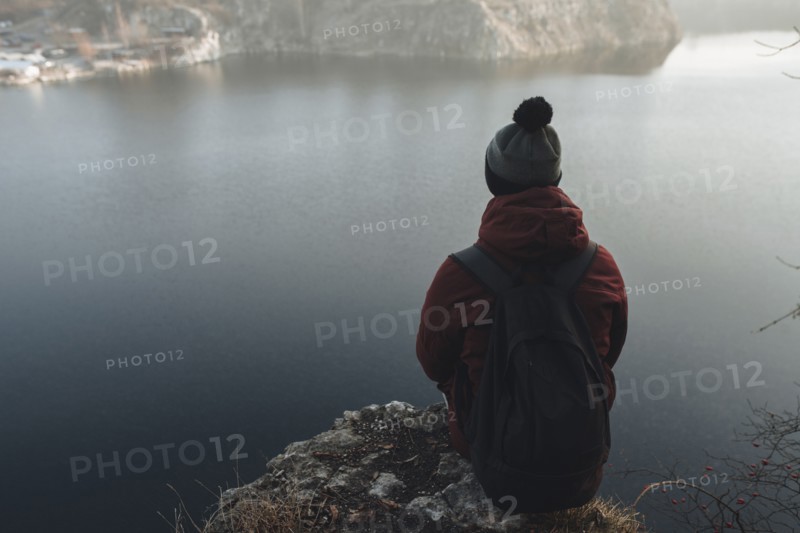 Caucasian man sitting at the edge of reservoir wearing backpack