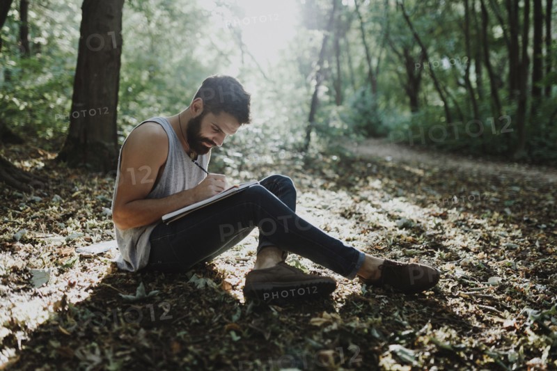 Caucasian man sitting in woods drawing on sketchpad