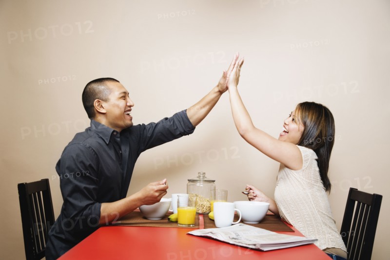 Asian couple high-fiving at breakfast table