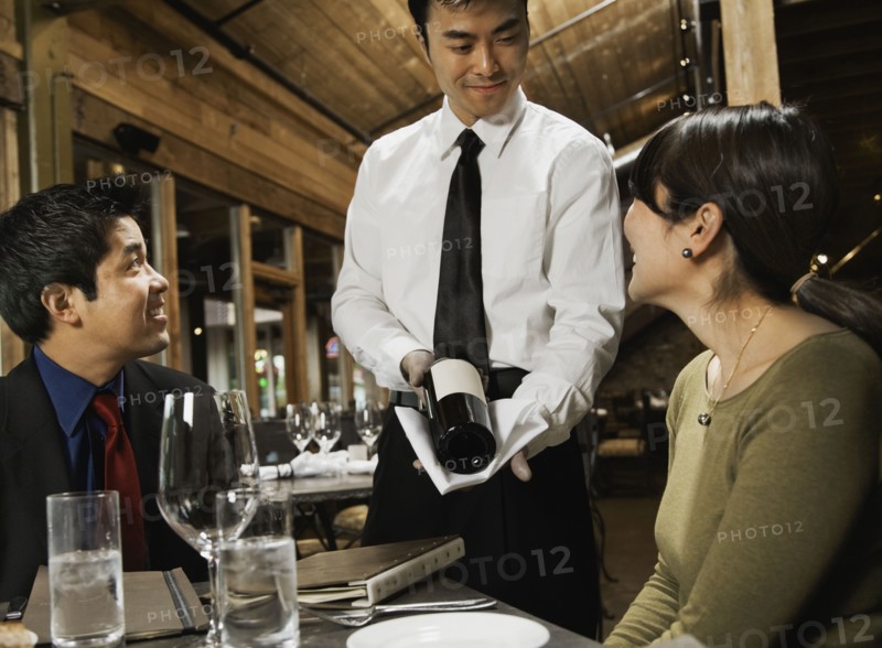 Asian waiter showing wine to couple