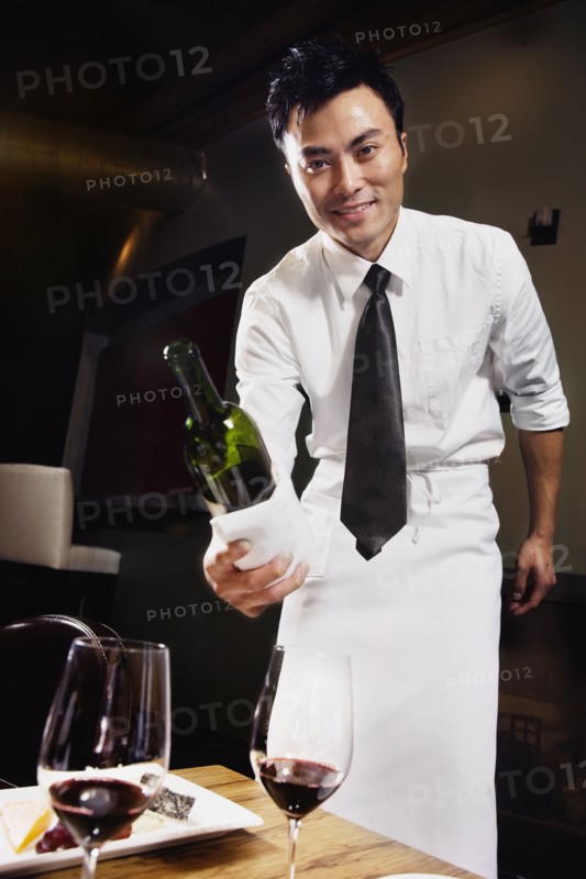 Asian waiter pouring wine