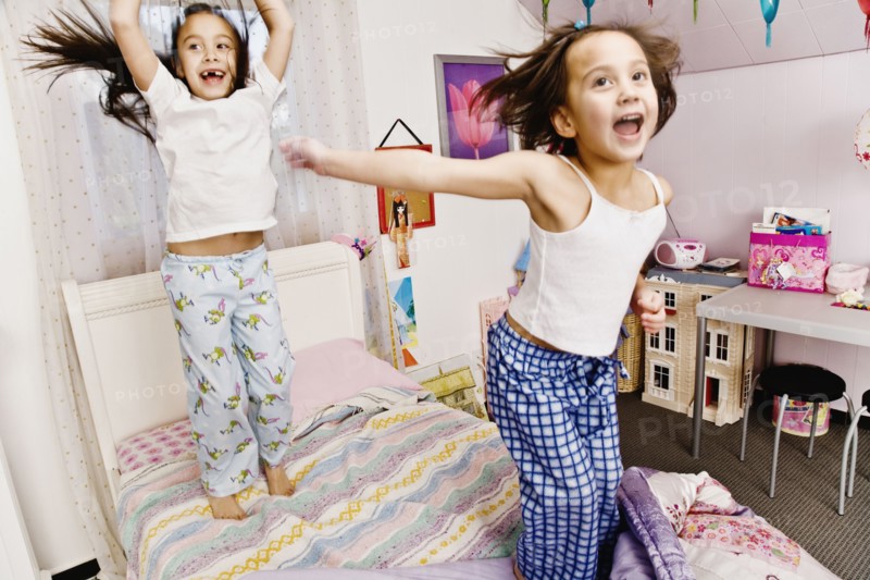 Asian sisters jumping on bed