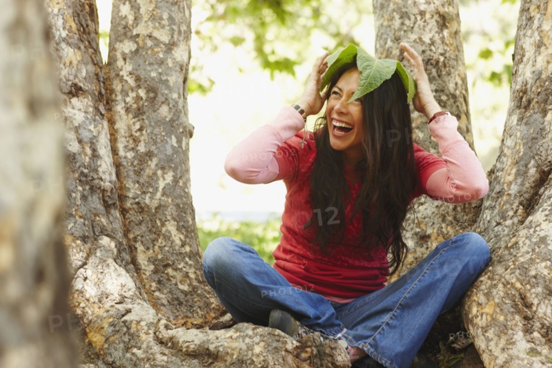 Hispanic woman sitting outdoors with leaf on her head