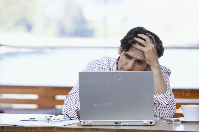 Hispanic businessman looking at laptop with hand on forehead
