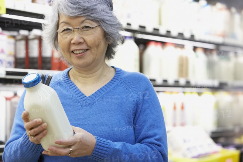 Senior Asian woman holding milk in grocery store