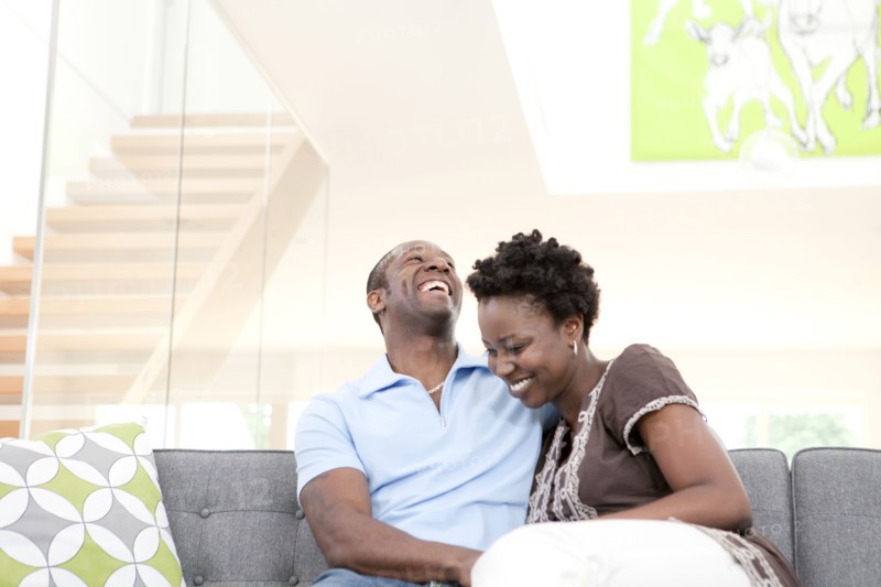 Laughing Black couple sitting on sofa in living room