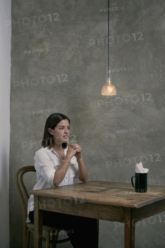 Serious Hispanic woman sitting at wooden table in corner