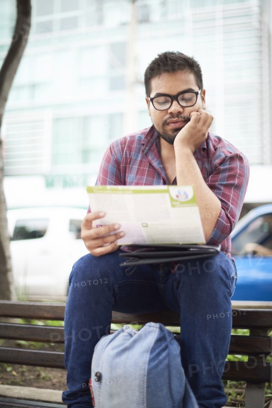Hispanic man sitting on top of bench reading brochure