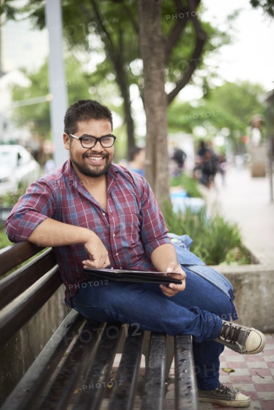 Smiling Hispanic man sitting on bench reading brochure