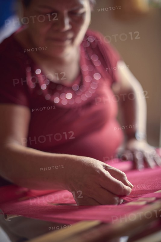 Hispanic woman weaving fabric on loom