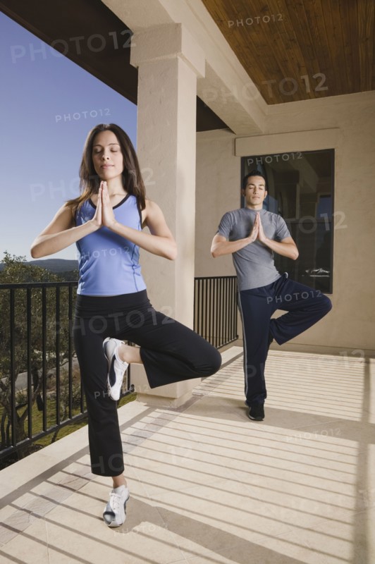 Hispanic couple doing yoga on balcony