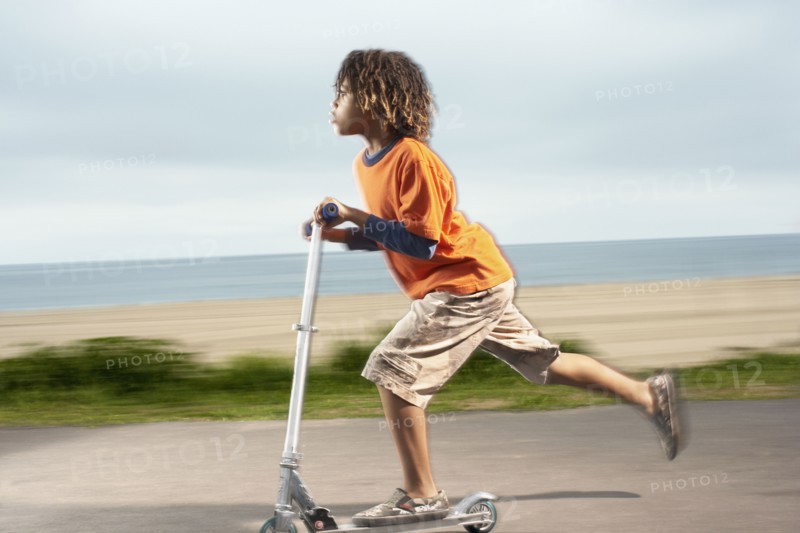 Mixed Race boy riding foot-powered scooter