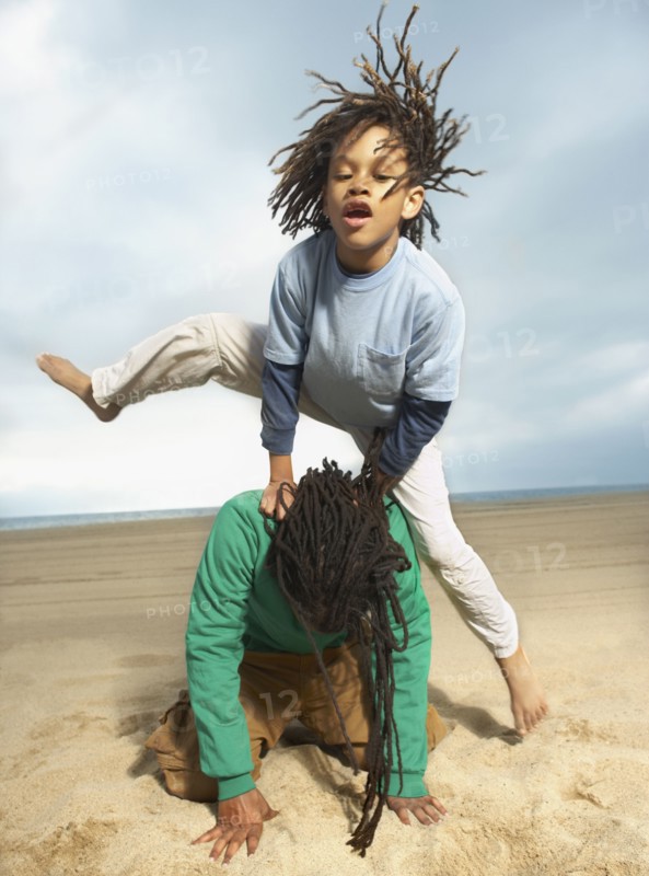 Mixed Race boy jumping over father on beach