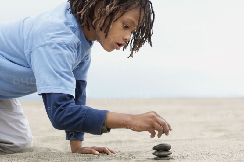Mixed Race boy stacking stones on sand