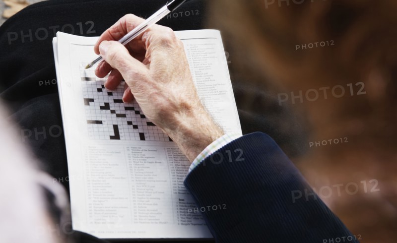 Close up of senior man's hand with pen on crossword puzzle