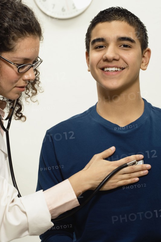 Female doctor checking young male patient with stethoscope