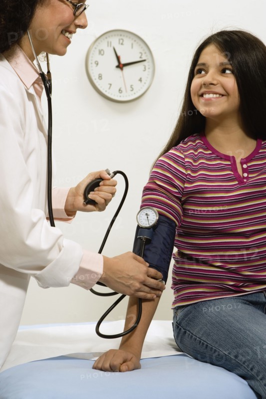 Female doctor taking young female patient's blood pressure