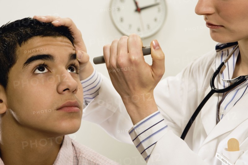 Female doctor checking young male patient's eye