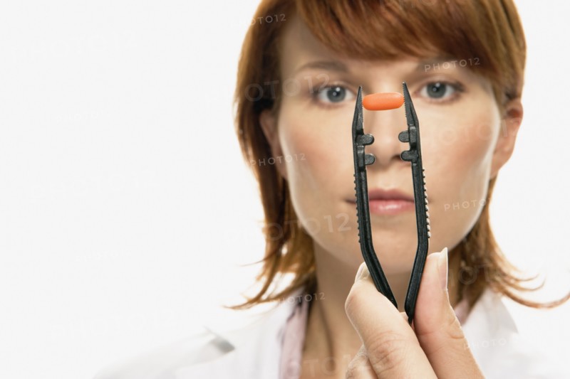 Woman holding pill in large tweezers