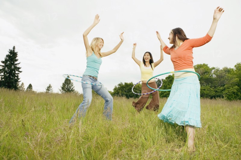 Three young women playing with plastic hoops in meadow