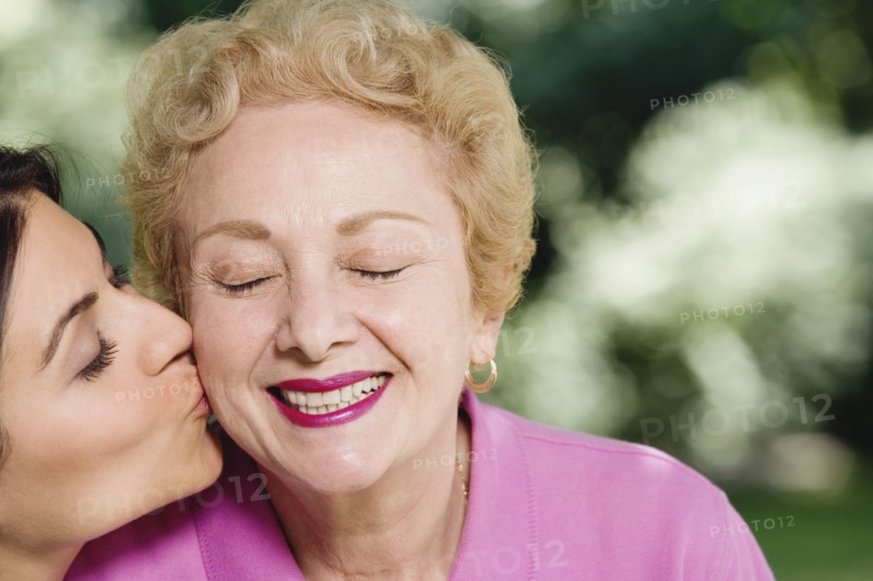 Hispanic woman kissing mother on cheek outdoors